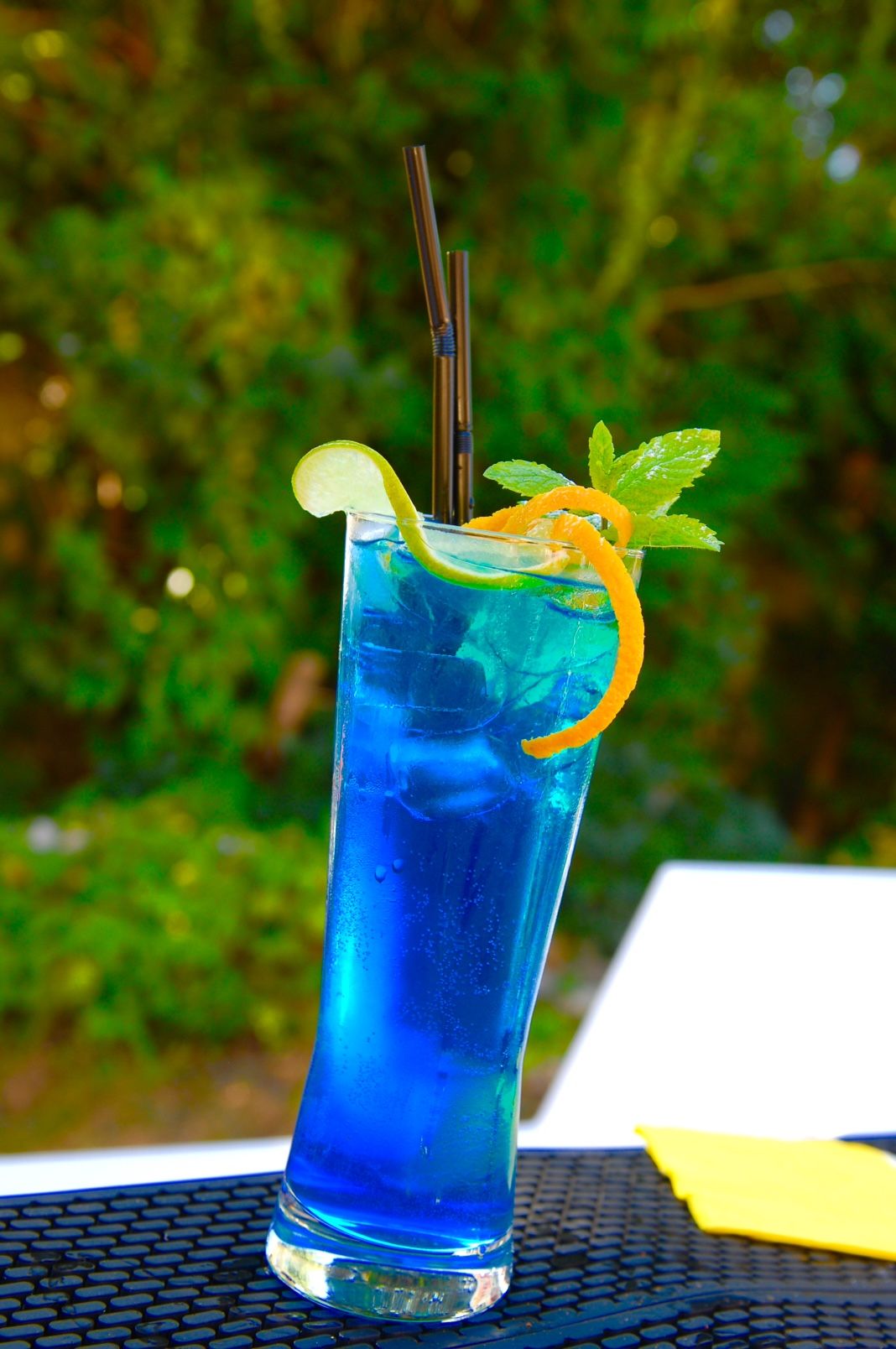 Cocktail bleu garni de menthe et d'agrumes servi en extérieur